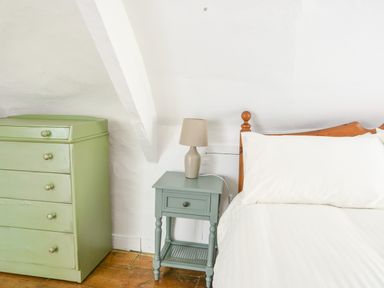 A bedroom with a wooden bed a green chest of drawers a blue side table and a table lamp at Braeside in Lyme Regis