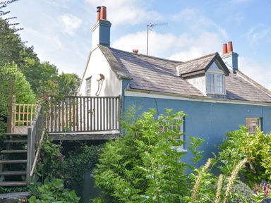 Exterior of a blue and white house with a tiled roof wooden deck and green plants in Lyme Regis