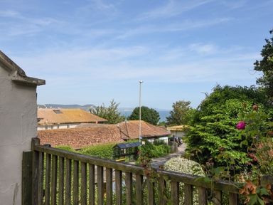 A view from a wooden balcony showing rooftops trees and a distant sea at Braeside in Lyme Regis