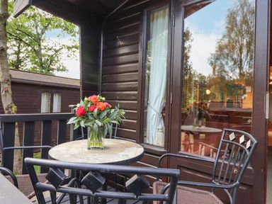A balcony with a stone table and metal chairs with red flowers on the table at Ennerdale Lodge in Burnside Park near Keswick
