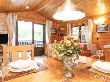 A dining area with wooden table set with plates glasses and a flower vase in a wooden cabin at Ennerdale Lodge Burnside Park near Keswick