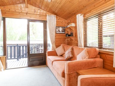 A sitting area with an orange sofa and cushions next to a window and glass door at Ennerdale Lodge Burnside Park near Keswick