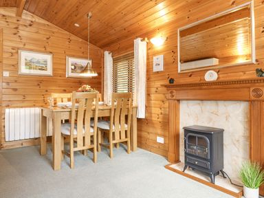 A dining area with wooden table and chairs next to a fireplace with a stove at Ennerdale Lodge Burnside Park near Keswick