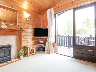 A wooden paneled living room with a fireplace television small tables and a door leading to a balcony at Ennerdale Lodge in Burnside Park near Keswick