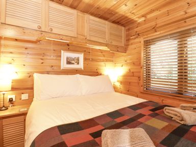 A bedroom with a bed white pillows wooden walls and a window with blinds at Ennerdale Lodge Burnside Park near Keswick