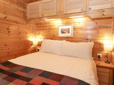 A bedroom with a double bed white pillows two bedside lamps wooden walls and cabinets at Ennerdale Lodge Burnside Park near Keswick