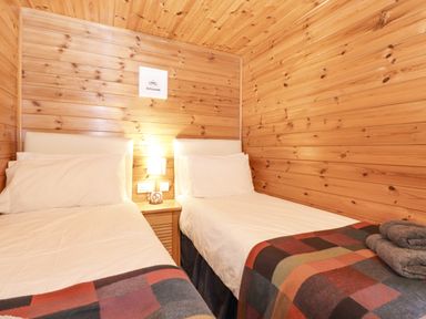 A bedroom with two single beds a bedside table with a lamp and wooden paneled walls at Ennerdale Lodge Burnside Park near Keswick