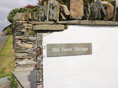 A stone wall with a metal sign reading Old Farm Cottage at Old Farm Cottage in Skelwith Fold
