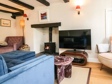 A living room with a blue sofa a fireplace and a television at Old Farm Cottage in Skelwith Fold