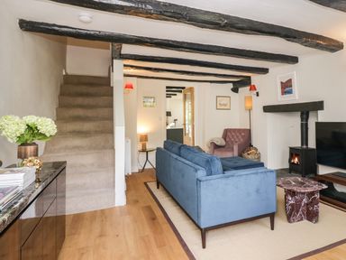A living room with a blue sofa a purple armchair a staircase and a wood stove at Old Farm Cottage Skelwith Fold