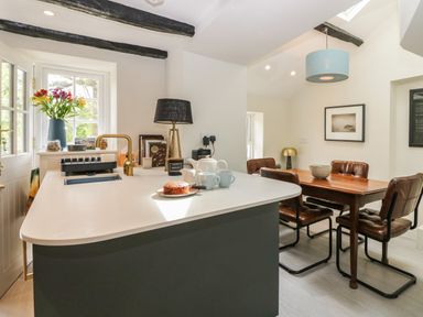 A kitchen island with a cake cups and a teapot next to a dining table with four chairs at Old Farm Cottage in Skelwith Fold