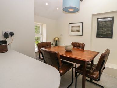 A dining area with a wooden table surrounded by four brown chairs a bowl on the table a blue hanging lamp two framed pictures on the wall and a small window at Old Farm Cottage Skelwith Fold