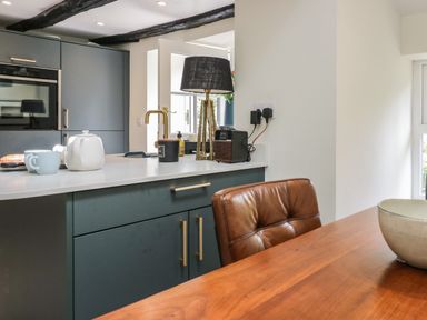 A kitchen with blue cabinets white countertop and a brown leather chair at Old Farm Cottage in Skelwith Fold