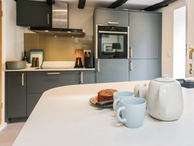 A kitchen with gray cabinets a built-in oven and a teapot with cups on the countertop at Old Farm Cottage in Skelwith Fold