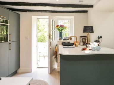 A kitchen with a door open to the outside and a countertop with a cake teapot cups and a lamp at Old Farm Cottage in Skelwith Fold