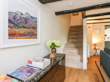 A hallway with carpeted stairs and a black marble top cabinet with books and flowers at Old Farm Cottage Skelwith Fold
