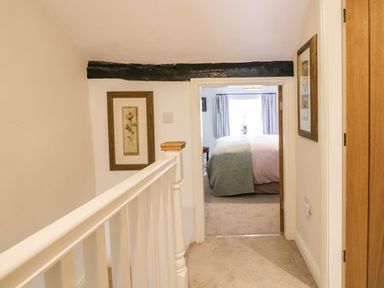 A hallway with a white banister and framed pictures leading to a bedroom at Old Farm Cottage in Skelwith Fold