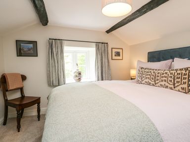 A bedroom with a bed a wooden chair and a window at Old Farm Cottage in Skelwith Fold
