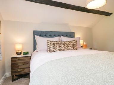 A bedroom with a bed with white bedding and decorative pillow two bedside tables with lamps and an alarm clock at Old Farm Cottage in Skelwith Fold