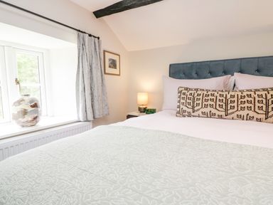 A bedroom with a bed a pillow a lamp a window with curtains and a decorative vase at Old Farm Cottage in Skelwith Fold