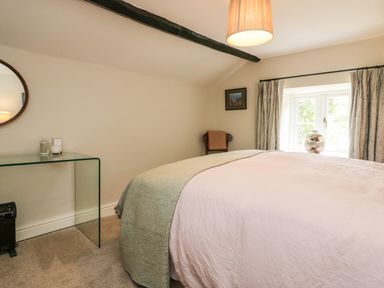 A bedroom with a bed near a window with curtains and a glass table with a mirror on the wall at Old Farm Cottage in Skelwith Fold