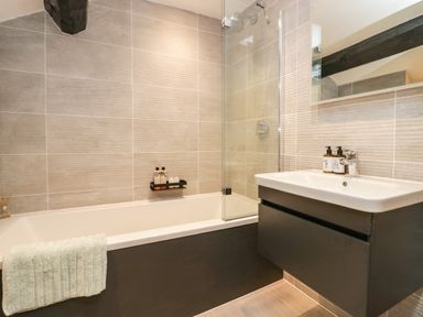 A bathroom with a bathtub, sink, mirror, and toiletries at Old Farm Cottage in Skelwith Fold
