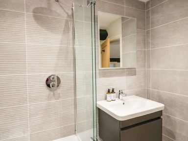 A bathroom with a sink drawer unit a mirror and a glass shower screen at Old Farm Cottage in Skelwith Fold