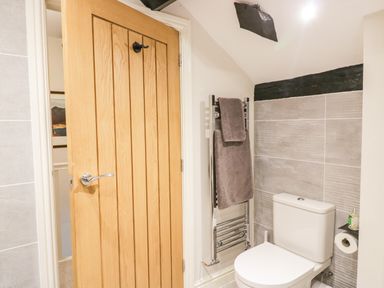 A bathroom with a wooden door a toilet a towel rack with towels and a toilet paper holder at Old Farm Cottage Skelwith Fold