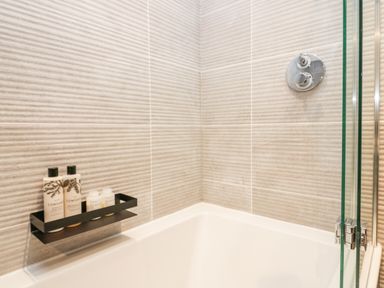 A bathtub corner with shampoo and conditioner bottles on a black shelf at Old Farm Cottage in Skelwith Fold