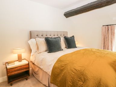 A bedroom with a bed with mustard bedspread and green cushions next to a bedside table with a lamp at Old Farm Cottage in Skelwith Fold