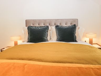 A bedroom with a bed with dark pillows and mustard and orange blankets with lamps on side tables at Old Farm Cottage in Skelwith Fold