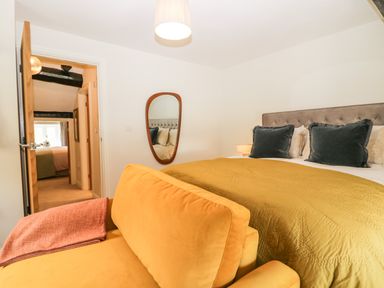 A bedroom with a yellow bedspread a yellow sofa and a wall mirror at Old Farm Cottage in Skelwith Fold