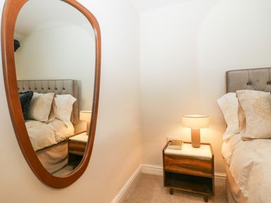 A bedroom corner with a bed a nightstand a lamp and a wall mirror at Old Farm Cottage in Skelwith Fold