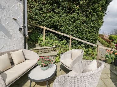 An outdoor seating area with wicker sofa and chairs around a table with flowers at Old Farm Cottage in Skelwith Fold