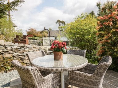 An outdoor patio with a round glass table surrounded by four wicker chairs and a potted plant on the table at Old Farm Cottage Skelwith Fold