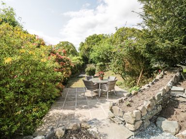 An outdoor patio with a round table and four chairs surrounded by bushes and trees at Old Farm Cottage in Skelwith Fold