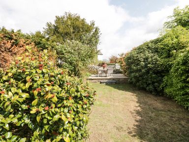 A garden with bushes a grassy area and a patio with a table and chairs at Old Farm Cottage in Skelwith Fold