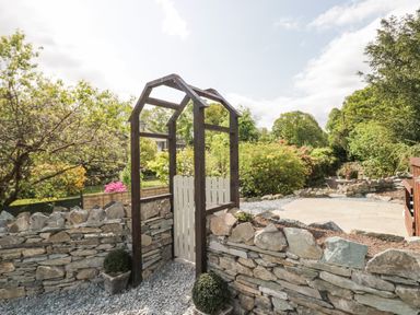 A stone garden wall with a wooden gate and trellis surrounded by greenery at Old Farm Cottage in Skelwith Fold