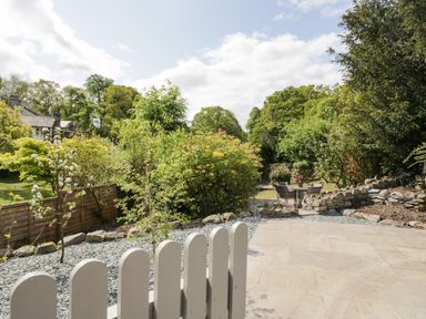 A garden with stone patio chairs and table surrounded by trees and bushes at Old Farm Cottage in Skelwith Fold