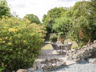 A garden patio with a round table and four chairs surrounded by trees and bushes at Old Farm Cottage in Skelwith Fold