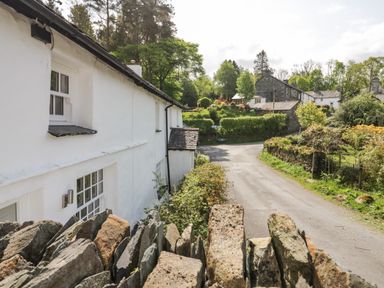 A country road with white cottages and stone walls surrounded by trees and greenery at Old Farm Cottage in Skelwith Fold