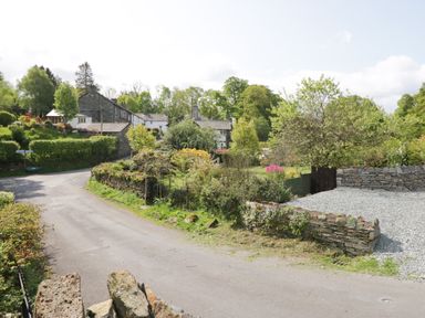 A rural road with stone walls trees and houses at Old Farm Cottage in Skelwith Fold