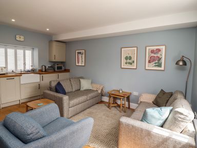 A living room with sofas, an armchair, side tables, wall art, and kitchen cabinets at Lark Rise in Alnmouth