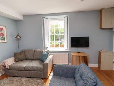 A living room with two sofas a wall-mounted TV and a window with shutters at Lark Rise in Alnmouth