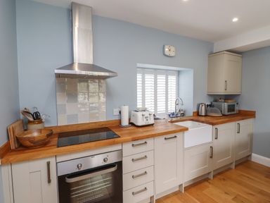 A kitchen with wooden countertops white cabinets a oven stovetop toaster and window shutters at Lark Rise in Alnmouth