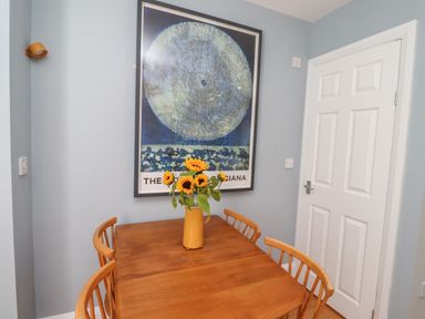 A wooden dining table with four chairs and a vase of sunflowers under a large framed artwork on a light blue wall in a room with a white door at Lark Rise in Alnmouth