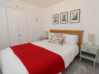 A bedroom with a wooden bed frame white bedding and red throw with two bedside tables and three framed pictures on the wall at Lark Rise in Alnmouth