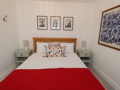 A bedroom with a wooden bed frame white bedding red blanket and decorative pillows two bedside tables with lamps and three framed pictures on the wall at Lark Rise in Alnmouth