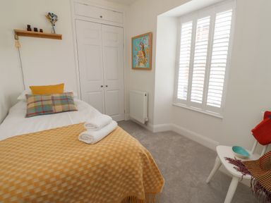 A bedroom with a single bed with pillows and a blanket next to a closet and a window with shutters at Lark Rise in Alnmouth