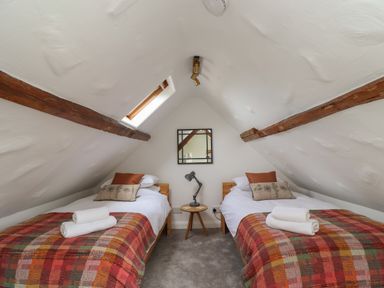 A small attic bedroom with two single beds a wooden side table and a ceiling window at Lark Rise in Alnmouth